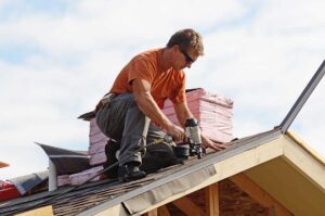 Homeowner inspecting gutters from the ground beneath a snow-free roof with mature trees nearby.