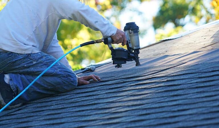 Homeowner examining aging asphalt shingles near a gutter while snow remains on the roof.