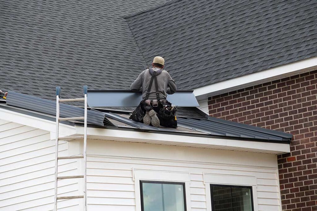 A residential roof showing asphalt shingles beside metal roofing panels under seasonal snow.
